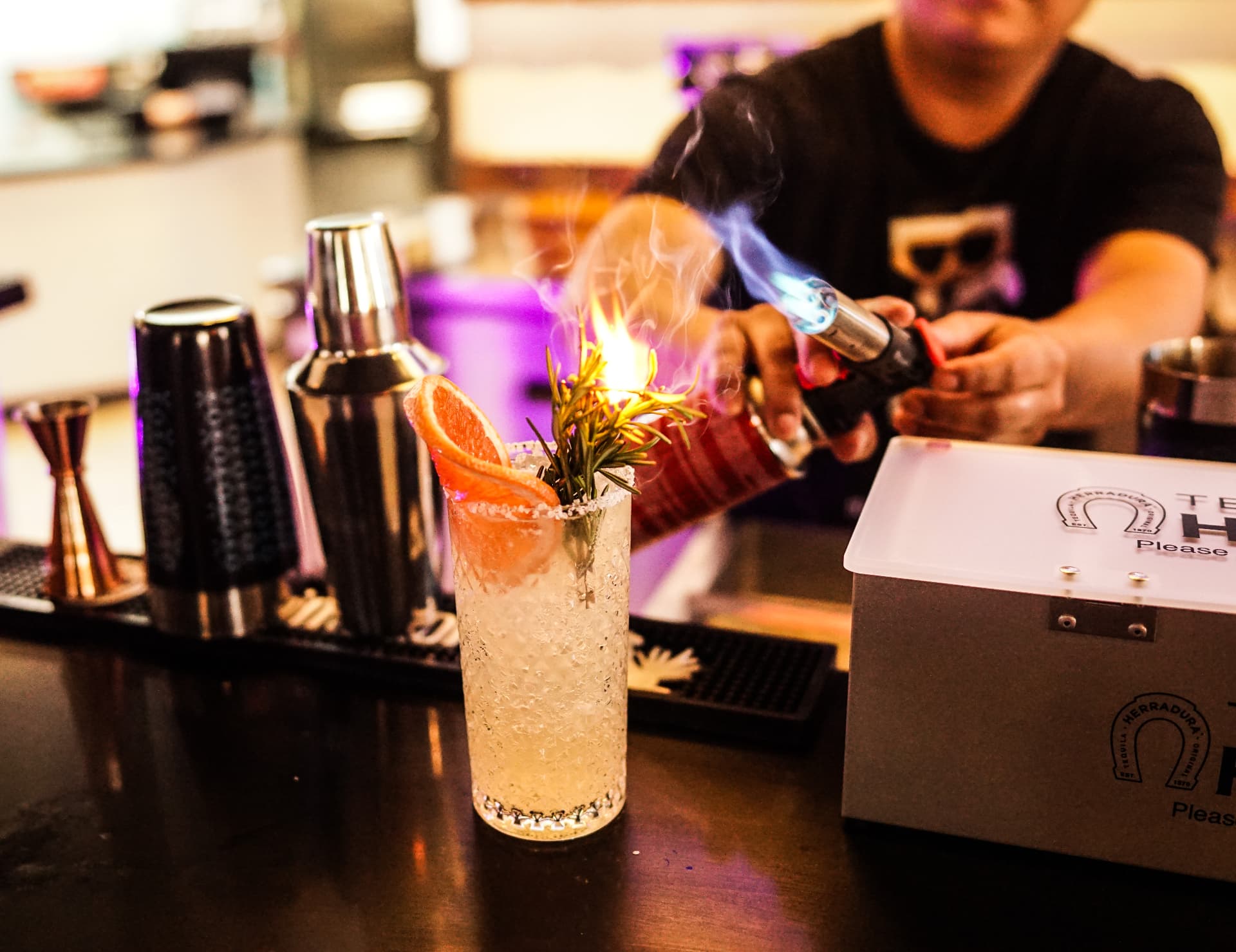 Bartender flames a rosemary sprig over a grapefruit tequila cocktail at the Soko bar